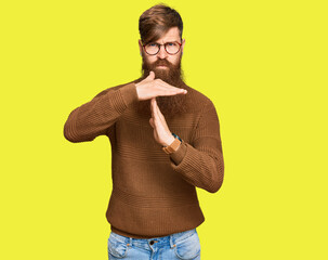 Young irish redhead man wearing casual clothes and glasses doing time out gesture with hands,...