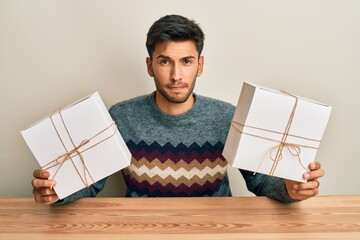 Young handsome man holding gifts skeptic and nervous, frowning upset because of problem. negative...