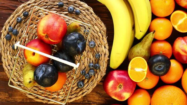 Fresh fruit rotating in a golden shopping basket next to it on a wooden background is a large amount of fruit. The concept of rising food prices or an incentive to buy healthy food 