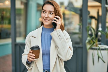 Young hispanic woman talking on the smartphone and drinking coffee at the city.