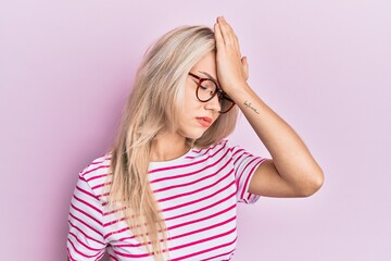 Beautiful caucasian blonde girl wearing casual clothes and glasses surprised with hand on head for mistake, remember error. forgot, bad memory concept.
