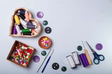 Wooden heart shaped box of multicolored beads and buttons, awl, scissors, crochets and spool of threads for sewing and embroidery. Set of materials for handcraft, making of bijouterie and accessories