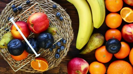 Fresh fruit rotating in a golden shopping basket next to it on a wooden background is a large amount of fruit. The concept of rising food prices or an incentive to buy healthy food 