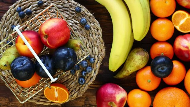 Fresh fruit rotating in a golden shopping basket next to it on a wooden background is a large amount of fruit. The concept of rising food prices or an incentive to buy healthy food 