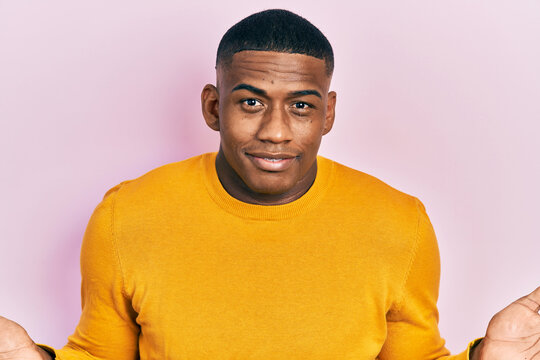 Young black man wearing casual yellow sweater clueless and confused with open arms, no idea and doubtful face.
