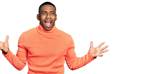 Young black man wearing orange turtleneck sweater crazy and mad shouting and yelling with aggressive expression and arms raised. frustration concept.