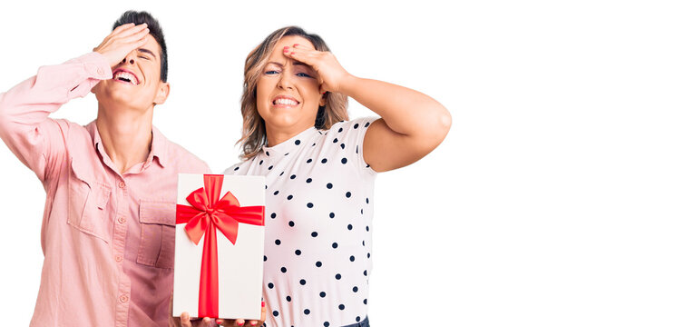 Couple of women holding gift stressed and frustrated with hand on head, surprised and angry face