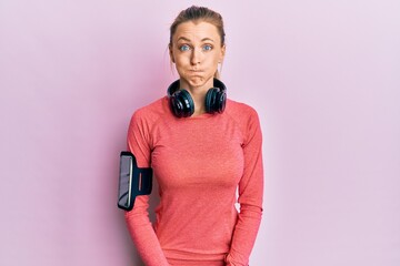 Beautiful caucasian woman wearing sportswear and arm band puffing cheeks with funny face. mouth...