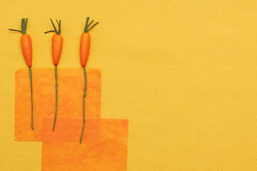 three imitation carrots on a background of orange textured translucent paper on a yellow fabric...