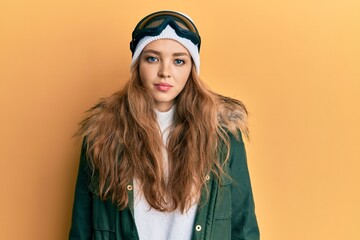 Beautiful blonde caucasian woman wearing snow wear and sky glasses with serious expression on face. simple and natural looking at the camera.