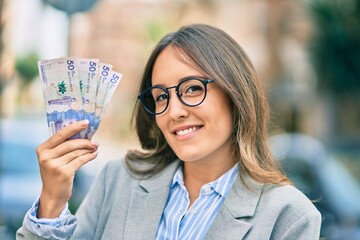 Young hispanic businesswoman smiling happy holding colombian 50 pesos banknotes at the city.