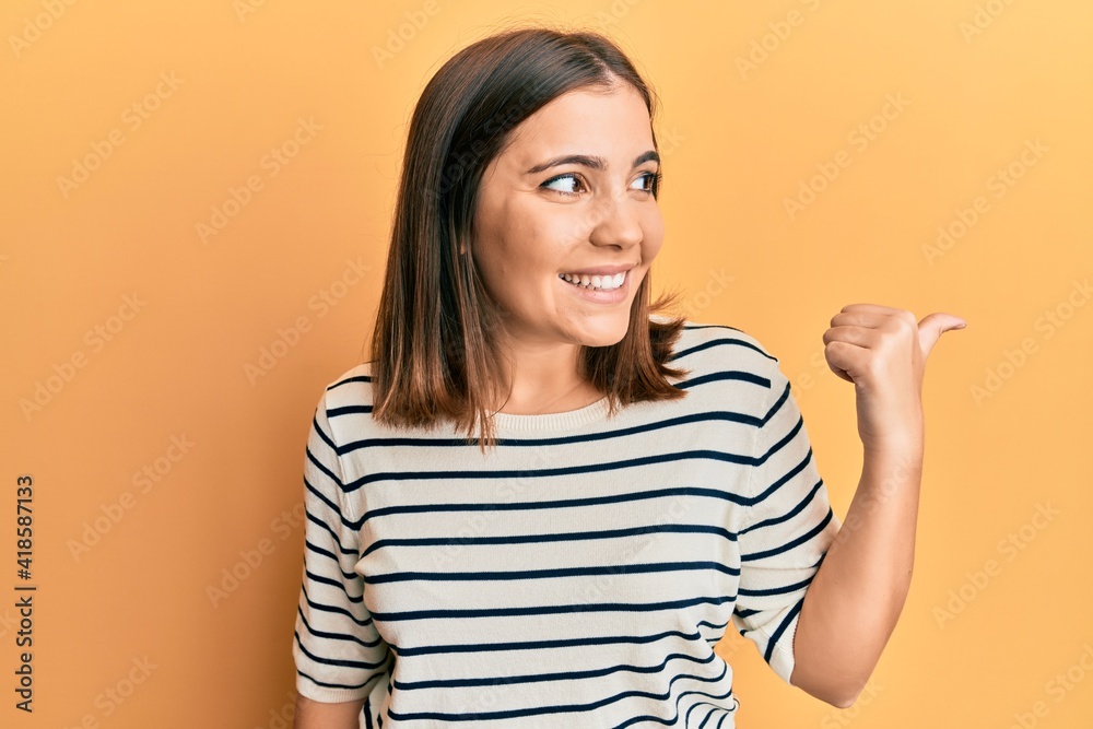 Sticker Young beautiful woman wearing casual striped t shirt pointing thumb up to the side smiling happy with open mouth