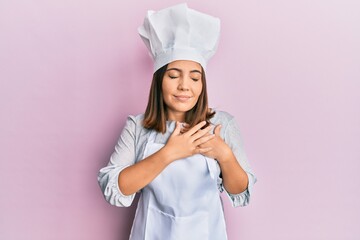 Young beautiful woman wearing professional cook uniform and hat smiling with hands on chest with closed eyes and grateful gesture on face. health concept.