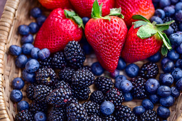 red strawberries with green leafy tops, surrounded by ripe blueberries and blackberries - 418587549