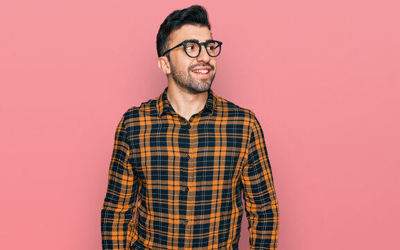 Hispanic man with beard wearing casual clothes and glasses looking away to side with smile on face, natural expression. laughing confident.