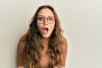 Young hispanic girl wearing casual clothes and glasses afraid and shocked with surprise and amazed...
