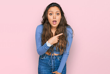 Young hispanic girl wearing casual clothes surprised pointing with finger to the side, open mouth amazed expression.