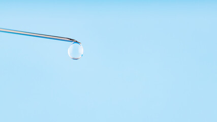 Vaccine drop on syringe needle. Vaccination concept, disease prevention. Needle with a drop of vaccine on a blue background. Coronavirus vaccine development
