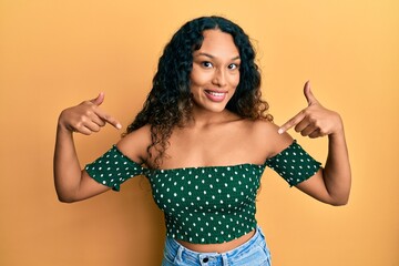 Young latin woman wearing casual clothes looking confident with smile on face, pointing oneself with fingers proud and happy.