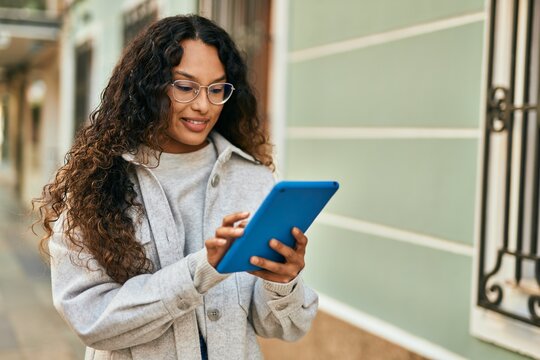 Young latin woman smiling happy using touchpad at the city.