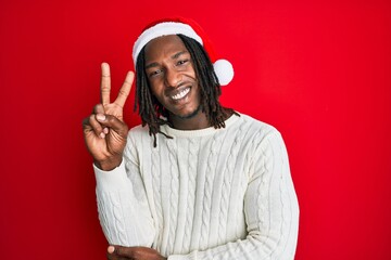 African american man with braids wearing christmas hat smiling with happy face winking at the...