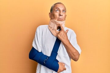 Handsome mature senior man wearing cervical collar and arm on sling thinking concentrated about...