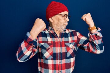 Handsome mature man wearing hipster look with wool cap showing arms muscles smiling proud. fitness...