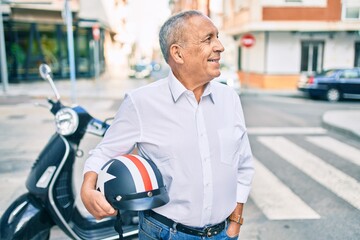 Senior motorcyclist man smiling happy holding moto helmet at the city.