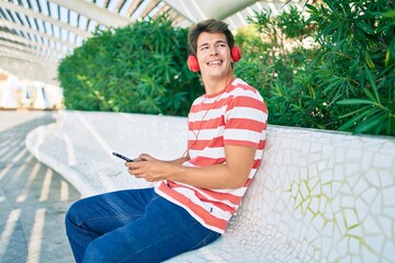 Fototapeta premium Young caucasian man smiling happy using smartphone and headphones sitting at the park.