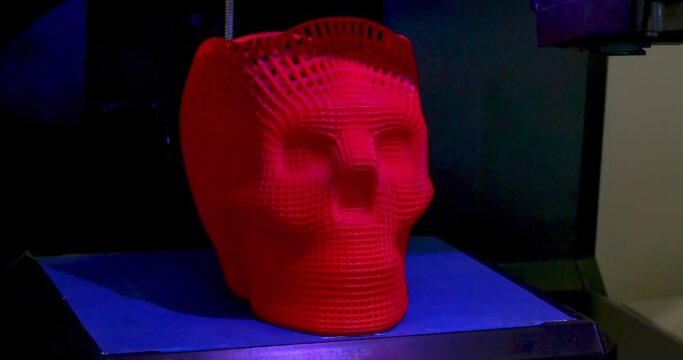 Skull printed with plastic of red color on a 3d printer. Inside 3d printer,