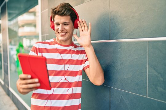 Young caucasian man smiling happy doing video call using touchpad and headphones at the city.