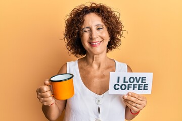 Beautiful middle age mature woman holding i love coffee banner winking looking at the camera with...