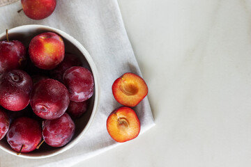 Ripe red plums in a white plate on marble background. Healthy food. 
