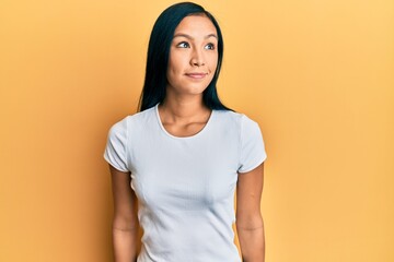 Obraz premium Beautiful hispanic woman wearing casual white tshirt smiling looking to the side and staring away thinking.