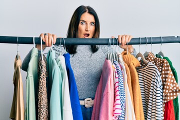 Middle age brunette woman working as professional personal shopper in shock face, looking skeptical and sarcastic, surprised with open mouth