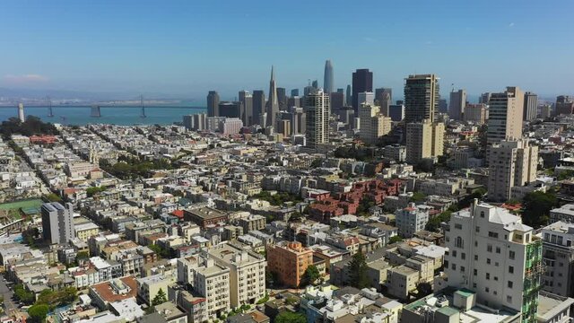 Aerial panning shot of cityscape by famous bridge over sea against blue sky, drone flying over modern city on sunny day - San Francisco, California