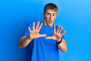 Young caucasian man wearing casual blue t shirt afraid and terrified with fear expression stop gesture with hands, shouting in shock. panic concept.