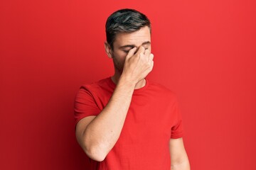 Handsome caucasian man wearing casual red tshirt tired rubbing nose and eyes feeling fatigue and headache. stress and frustration concept.