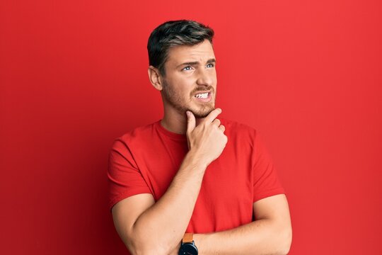 Handsome caucasian man wearing casual red tshirt thinking worried about a question, concerned and nervous with hand on chin