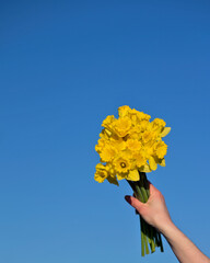 girl's hand holding bouquet of yellow flowers on blue sky background