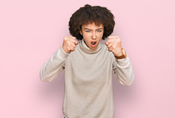 Young hispanic girl wearing wool winter sweater angry and mad raising fists frustrated and furious...