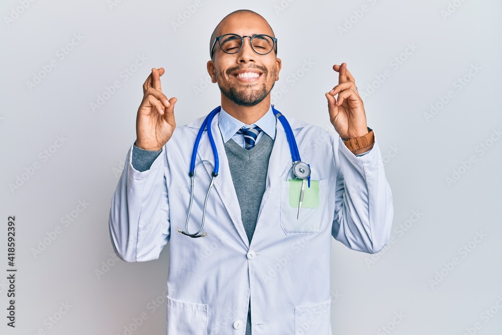 Sticker Hispanic adult man wearing doctor uniform and stethoscope gesturing finger crossed smiling with hope and eyes closed. luck and superstitious concept.