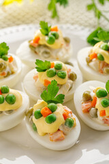 Easter boiled eggs stuffed with vegetable salad with mayonnaise served on a white plate close up view