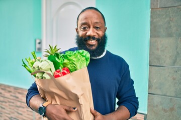 African american man with beard holding paper bag of groceries from supermarket