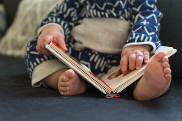 Young baby reading board book; closeup of dimpled hands and chubby feet