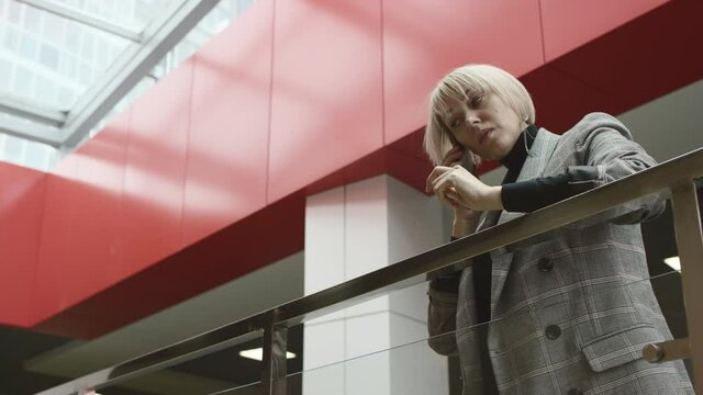 A side view slow motion close up of a blonde business woman leaning on a rail and recieving a call from her colleague on the phone