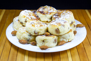 Ukrainian syrnyky or cheese pancakes with raisins, served with sugar powder and almond seeds on a white plate on dark background, ukrainian cuisine concept