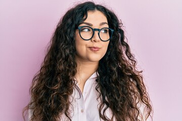 Obraz premium Young brunette woman with curly hair wearing casual clothes and glasses smiling looking to the side and staring away thinking.
