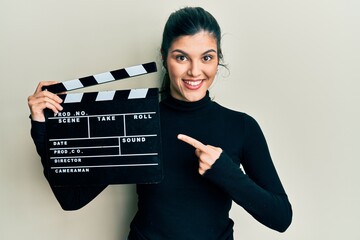 Young hispanic woman holding video film clapboard smiling happy pointing with hand and finger
