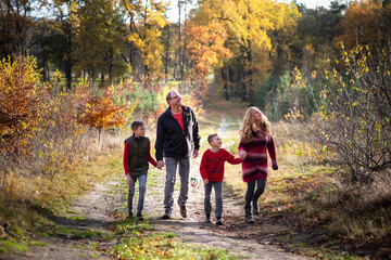 Fototapeta premium Eine glückliche, vierköpfige Familiegeht über dem langen Weg im Herbstwald und schauen sich um, Genießen die Natur und Herbstfarben